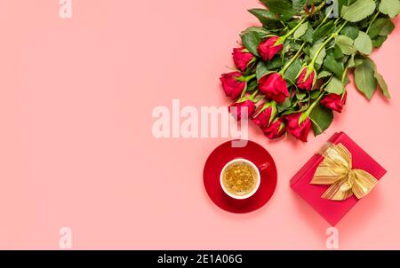 Roter Rosenstrauß, Geschenkbox mit goldenem Bogenknoten und Kaffeetasse auf rosa Hintergrund. Geburtstag, Mütter, Frauen oder Valentinstag Feier. Liebe Stockfoto