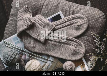 Ein Paar von Hand gestrickte Socken mit Garn Ball und Stricknadeln. Natürliche Farben. Dunkler rustikaler Holzhintergrund. Stockfoto