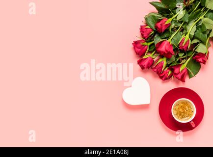 Roter Rosenstrauß, weißes Herz und Tasse Kaffee auf rosa Hintergrund. Geburtstag, Mütter, Frauen oder Valentinstag Feier. Liebe und Dating-Konzept Stockfoto