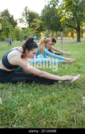 Vertikale Aufnahme von drei jungen Frauen, die sich im Freien strecken und gemeinsam im Park Yoga machen Stockfoto