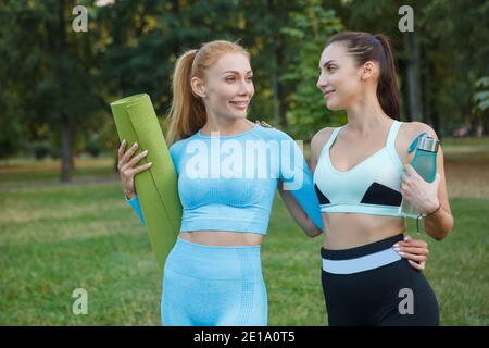 Glückliche, gesunde Freundinnen, die nach dem Training im Freien im Park spazieren, lächeln und fröhlich plaudern Stockfoto