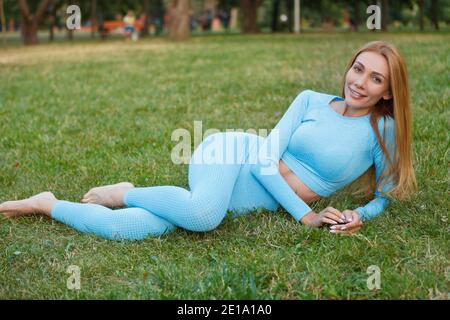 Ganzkörperaufnahme einer schönen, gesunden und gesunden Frau In Sportkleidung, die auf dem Rasen im Park liegt Stockfoto
