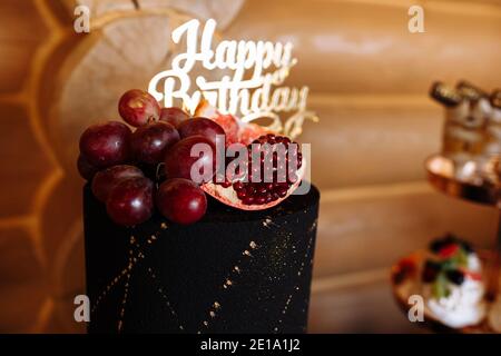 Große schwarze Geburtstagstorte mit frischem Obst und Süßigkeiten auf einem festlichen Tisch. Süßigkeitenbar. Tisch mit verschiedenen Süßigkeiten für Party. Stockfoto