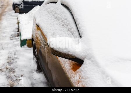 Schmutzige Autoseite mit dicken Schneeschichten bedeckt. Kalter Zyklon. Transportschwierigkeiten bei Schneefall Stockfoto