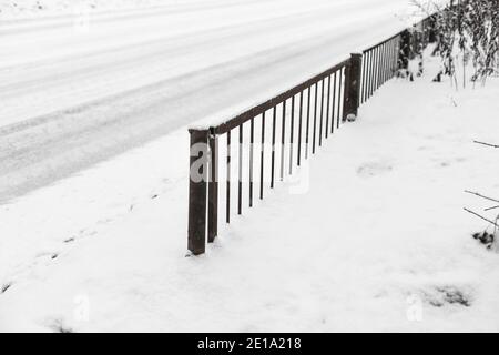 Metallischer rostiger Zaun am Straßenrand bei Schneefall. Selektiver Fokus. Kalter Zyklon Stockfoto