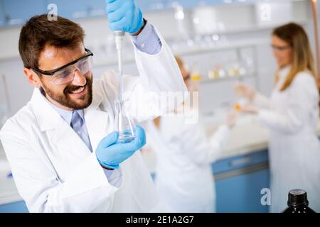 Hübscher junger Forscher in schützender Arbeitskleidung im Labor stehen Und Analyselflasche mit Flüssigkeit Stockfoto
