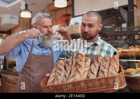 Junger männlicher Bäcker, der mit seinem Senior in der Bäckerei arbeitet Vater Stockfoto