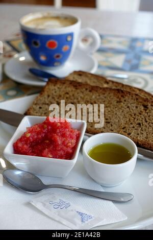 Traditionelles spanisches Frühstück mit geröstetem Brot, zerkleinerten Tomaten, nativem Olivenöl extra und einer Tasse Kaffee im Hintergrund in Sevilla, Andalusien. Stockfoto