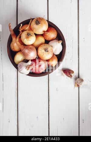 Zwiebeln und Knoblauch in einer Schüssel auf weißem Holzhintergrund, Draufsicht. Stockfoto