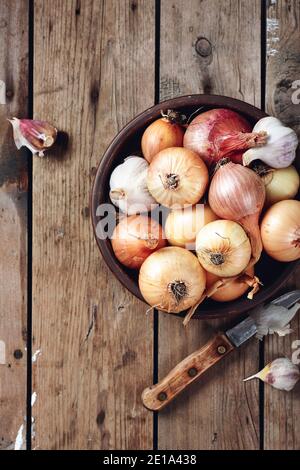 Gelbe, rote Zwiebeln und Knoblauch in einer Schüssel auf Holzgrund. Stockfoto