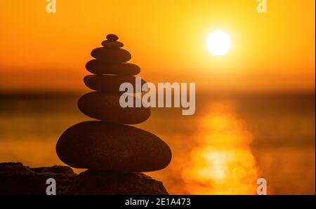 Ausgewogene Kieselsteinpyramide Silhouette am Strand. Abstrakt warmen Sonnenuntergang Bokeh mit Meer auf dem Hintergrund. Zen-Steine am Meer Strand, Meditation, Spa Stockfoto