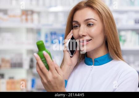 Freundliche Apothekerin, die telefonische Bestellungen entgegennimmt und in der Apotheke arbeitet. Fröhliche Chemikerin ruft ihre Patienten an und berät über Medikamente. C Stockfoto