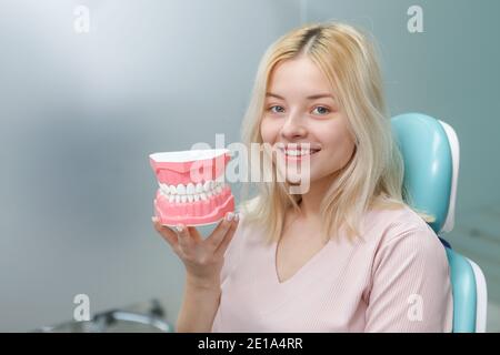 Glückliche junge Frau mit weißen gesunden Zähnen halten Kiefer Modell Sitzen im Zahnarztstuhl Stockfoto