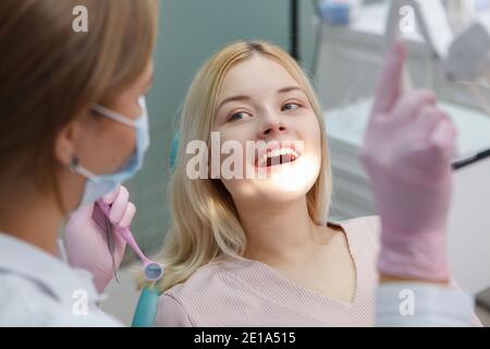 Fröhliche junge Frau lächelt während zahnärztliche Untersuchung durch professionelle Zahnarzt Stockfoto