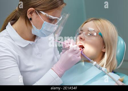 Junge Frau trägt Schutzbrille, während Zahnarzt ihre Zähne untersucht Stockfoto