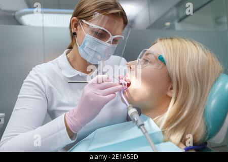 Weibliche Zahnärztin trägt Schutzmaske Gesicht, Behandlung der Zähne der weiblichen Patienten Stockfoto