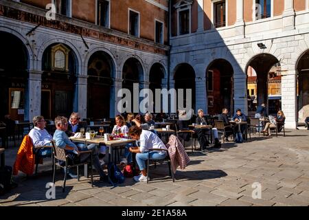 Touristen/Besucher entspannen sich in der Sonne in EINEM Café in der Nähe der Rialtobrücke, Venedig, Italien. Stockfoto