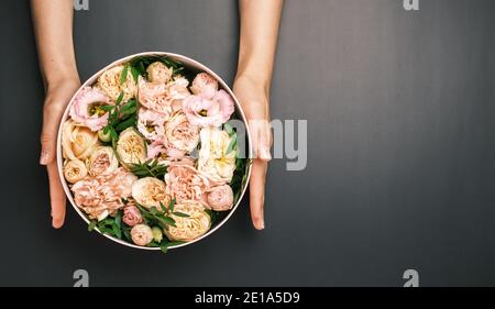 Rosa Geschenkbox mit einer floralen Komposition in Frauenhand auf dem schwarzen Hintergrund mit Kopierraum. Geschenk zum Valentinstag, Internationale Frauen Stockfoto