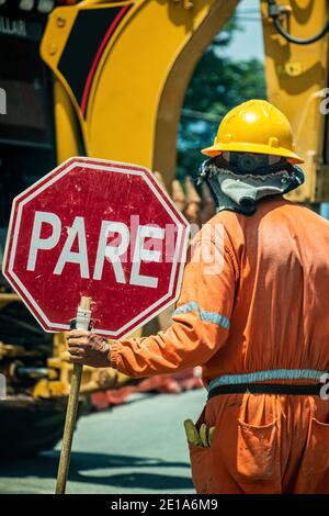 Ein Mann hält ein Stoppschild an der Baustelle, um Menschen zu warnen, die in der Nähe vorübergehen Stockfoto