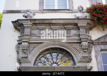 Architektonisches Detail eines alten Gebäudes in der Düsseldorfer Altstadt mit dekorativer Steinfigur und roten Blumen. Stockfoto