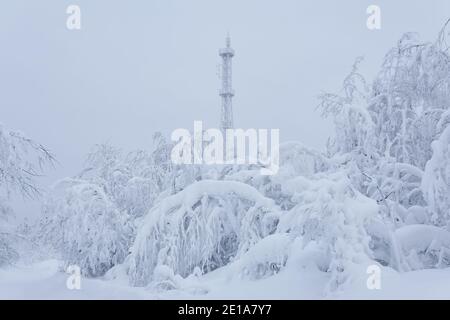 Eisbedeckte Zelle Turm über einem verschneiten Wald auf Ein Berg gegen einen Winterhimmel Stockfoto