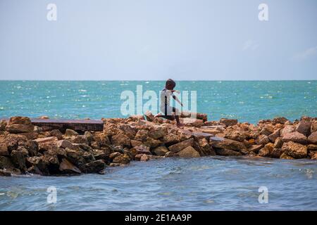 Boy genießt das frische Wasser an einem ruhigen Strand Springen von den Felsen zum Wasser Stockfoto