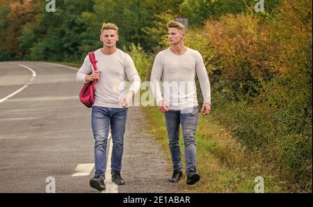 Jungs, die auf der Straße unterwegs sind. Automatischer Stopp für Reisende. Probleme werden transportiert. Wählen Sie Ort, wo Auto leicht zur Seite ziehen kann. Männer Rucksack zu Fuß Straße. Zwillinge gehen die Straße entlang. Adventure Concept. Stockfoto