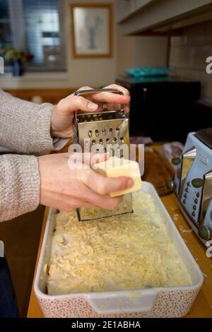 Reiben von Cheddar-Käse auf Lasagne-Teller Stockfoto