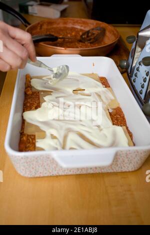 Lasagne Käsesauce über rohe Pasta verteilen. England Stockfoto