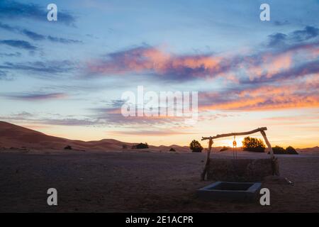 Ein Sonnenaufgang Blick auf einen traditionellen Brunnen und die Wüste Sanddünen von Erg Chebbi aus dem Dorf Merzouga. Stockfoto