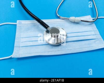 Schwarzes Stethoskop auf Einweg-Gesichtsmaske auf blauem Hintergrund. Medizinisches Konzept. Stockfoto