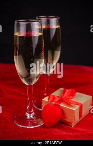 Zwei Gläser mit Champagner, goldener Geschenkbox und romantischem Dekor auf schwarzem und rotem Hintergrund Stockfoto