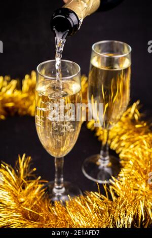 Zwei Gläser mit Champagner mit goldenem weihnachtlichen Lametta Dekor auf Schwarzer Hintergrund Stockfoto