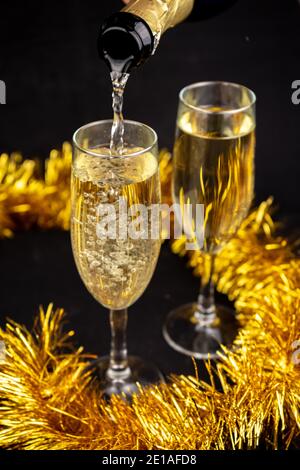 Zwei Gläser mit Champagner mit goldenem weihnachtlichen Lametta Dekor auf Schwarzer Hintergrund Stockfoto
