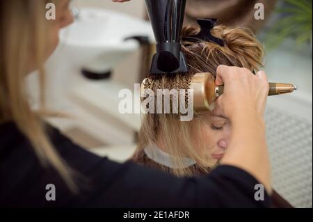Nahaufnahme eines Friseurs Bürsten Frau blonde Haare mit einem Haartrockner und professionelle Rundbürste Stockfoto