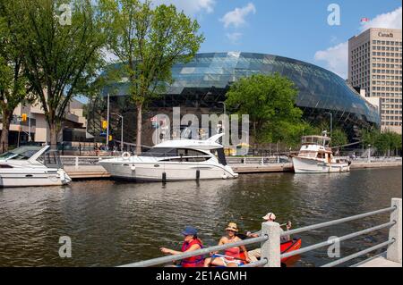 Ottawa, Kanada - 4. August 2012: Die Leute paddeln auf dem Rideau Kanal mit dem Shaw Centre, einem Kongresszentrum im Hintergrund. Stockfoto