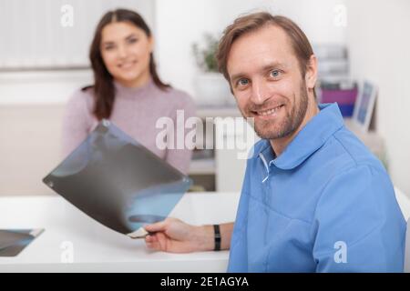 Glücklich reifen männlichen Arzt lächelt an die Kamera, hält Röntgenscan seiner weiblichen Patientin Stockfoto