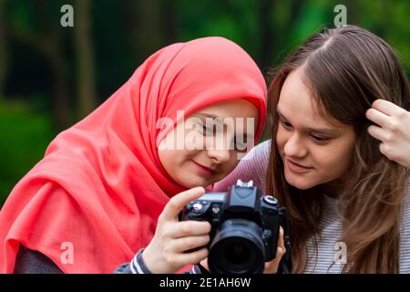 Junge muslimische Mädchen beobachten Fotos auf der professionellen Kamera. Freunde, Freundschaft, Schwestern, zusammen, Glück in der Natur Stockfoto