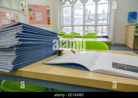 Stapel von Schulbüchern, auf einem Schreibtisch, den ein Lehrer markiert, in einem leeren Primärraum, mit rotem Stift. London, Großbritannien. Stockfoto