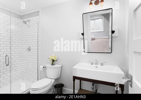 Ein luxuriöses, modernes Bauernhaus-Badezimmer mit einem neigbaren Spiegel, einem Standwaschbecken und einer weißen, mit U-Bahn gefliesten Dusche. Stockfoto