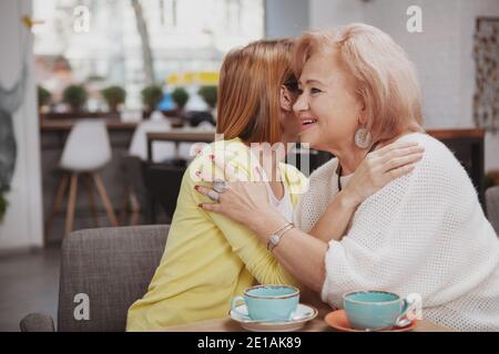 Glückliche ältere Mutter und ihre Erwachsene Tochter umarmten im Café. Ältere Frau, die ihr erwachsenes Kind im Café trifft Stockfoto