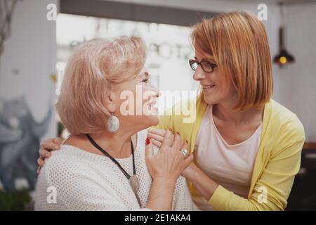 Reife Frau lächelt freudig und umarmt ihre ältere Mutter im Café Stockfoto
