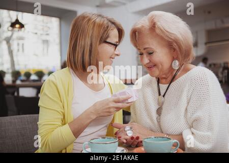 Frau mittleren Alters gratulierte ihrer älteren Mutter und gab ihr eine Geschenkbox. Ältere Mutter erhält ein Geschenk von ihrem erwachsenen Erwachsenen Stockfoto