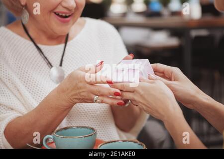Nahaufnahme einer glücklichen älteren Frau, die lachend eine Geschenkbox von ihrer Tochter erhielt. Ältere Frau bekommt Geburtstagsgeschenk Stockfoto