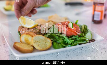 Nahaufnahme von Lachs-Tarte mit schön geschnittenen Tomatenblume in Tablett gesetzt, Köche Hand kann sorgfältig Platzierung einer halben Zitrone auf gesehen werden. Stockfoto
