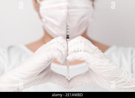 Nahaufnahme von Arzt oder Krankenschwester tragen weiße Handschuhe, eine Herzform mit den Händen, halten eine Spritze mit einem Tropfen in der Spitze der Nadel, in weiß BA Stockfoto