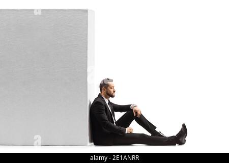 Nachdenklicher Geschäftsmann sitzt auf dem Boden und lehnt sich an ein Wand isoliert auf weißem Hintergrund Stockfoto