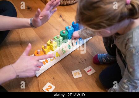 Eine Mutter, die ihre Finger hochhält, um ihrer zweijährigen Tochter zu zeigen, welche Nummer sie platzieren soll, indem sie ein Lernspielzeug mit Zählformen verwendet Stockfoto