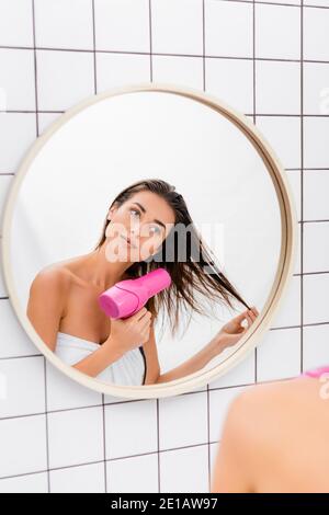 Junge Frau, die im Spiegel beim Trocknen der Haare im Badezimmer, verschwommen Vordergrund Stockfoto