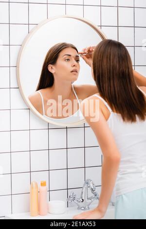 Junge Frau in Singlet zetting Augenbrauen in der Nähe Spiegel im Badezimmer Stockfoto